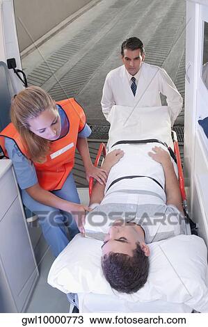 Paramedics leading a patient on a gurney into an ambulance View Large Photo Image Stock Image - Paramedics leading a patient on a gurney into an ambulance. Fotosearch