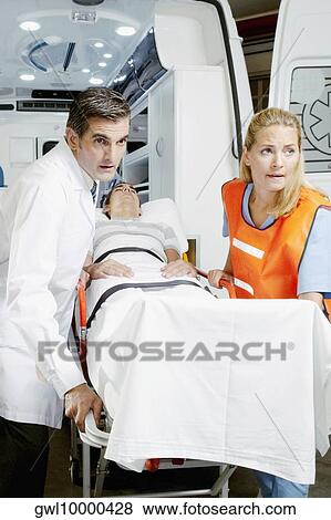 Paramedics pushing a patient on a gurney from an ambulance View Large Photo Image Stock Photo - Paramedics pushing a patient on a gurney from an ambulance. Fotosearch