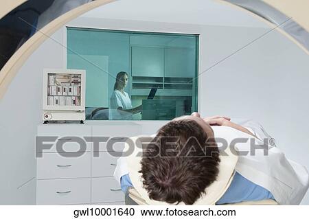 Patient going through an MRI scan with a doctor analyzing an X-Ray report in background View Large Photo Image Stock Image - Patient going through an MRI scan with a doctor analyzing an X-Ray report in background. Fotosearch