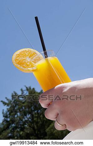 Person's hand holding a glass of orange juice View Large Photo Image Picture - Person's hand holding a glass of orange juice. Fotosearch