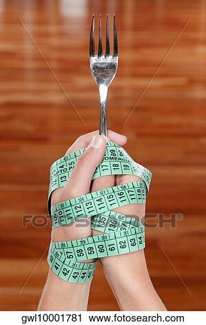 Stock Image - Person's hands wrapped with a tape measure holding a fork. Fotosearch