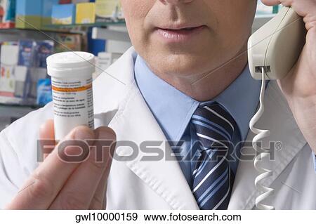 Pharmacist holding a medicine bottle and talking on the telephone View Large Photo Image Stock Photo - Pharmacist holding a medicine bottle and talking on the telephone. Fotosearch