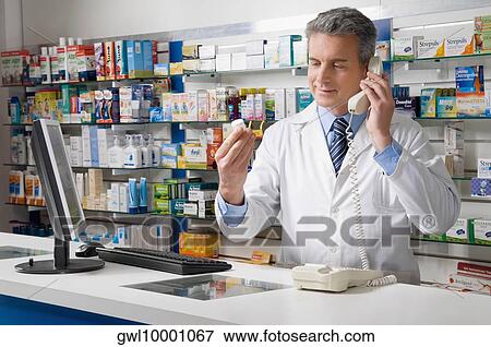 Stock Photo - Pharmacist looking at a drug bottle and talking on the telephone. Fotosearch