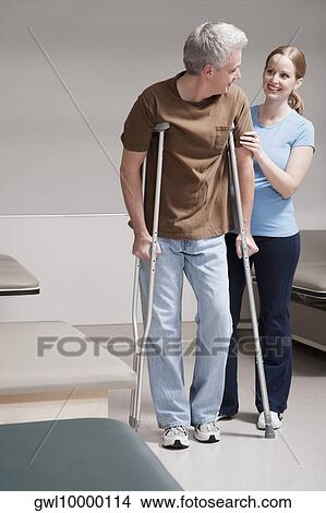 Physiotherapist assisting a patient in walking with crutches View Large Photo Image Picture - Physiotherapist assisting a patient in walking with crutches. Fotosearch