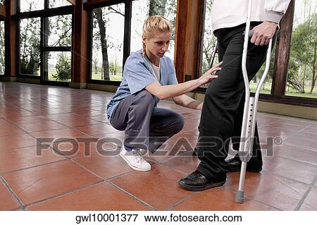 Stock Photo - Physiotherapist assisting a woman in walking. Fotosearch