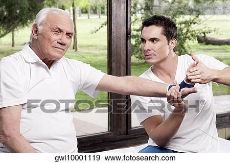 Stock Photo - Physiotherapist examining a man's hand. Fotosearch