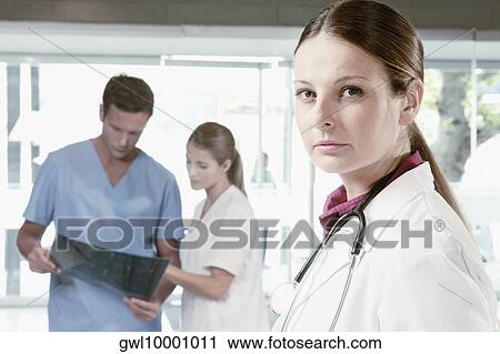Portrait of a female doctor with her colleagues examining an X-Ray in the background View Large Photo Image Stock Image - Portrait of a female doctor with her colleagues examining an X-Ray in the background. Fotosearch