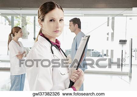 Stock Photograph - Portrait of a female doctor with her colleagues discussing in the background. Fotosearch