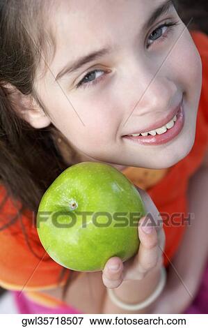 Stock Photo - Portrait of a girl showing a granny smith apple and smiling. Fotosearch