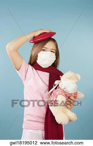Stock Image - Portrait of a girl wearing a flu mask and applying an ice pack on her head. Fotosearch