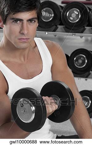 Stock Photo - Portrait of a man exercising with dumbbell in a gym. Fotosearch