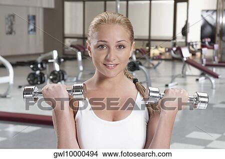 Picture - Portrait of a woman exercising with dumbbell in a gym. Fotosearch