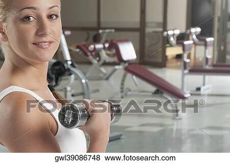 Portrait of a woman exercising with dumbbell in a gym View Large Photo Image Stock Photo - Portrait of a woman exercising with dumbbell in a gym. Fotosearch