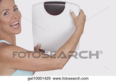 Stock Photo - Portrait of a woman holding a bathroom scale and laughing. Fotosearch