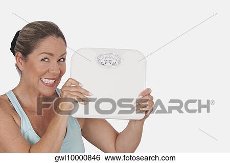Portrait of a woman holding a bathroom scale and smiling View Large Photo Image Stock Photograph - Portrait of a woman holding a bathroom scale and smiling. Fotosearch