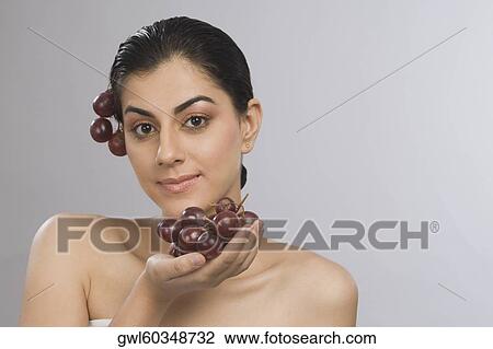 Stock Image - Portrait of a woman holding a bunch of red grapes. Fotosearch