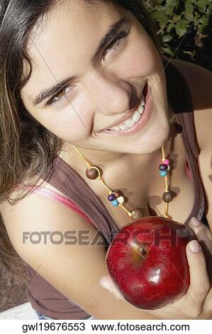 Stock Image - Portrait of a woman holding an apple and smiling. Fotosearch