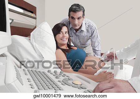 Pregnant woman going through an ultrasound scan with her husband beside her View Large Photo Image Stock Photo - Pregnant woman going through an ultrasound scan with her husband beside her. Fotosearch