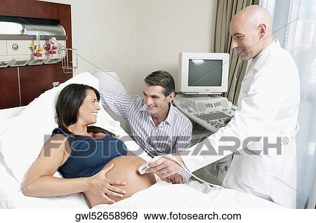 Stock Photo - Pregnant woman going through an ultrasound scan with her husband beside her. Fotosearch