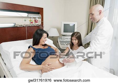 Stock Photograph - Pregnant woman going through an ultrasound scan with her daughter looking at her. Fotosearch