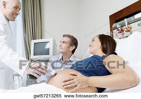 Pregnant woman going through an ultrasound scan with her husband beside her View Large Photo Image Stock Photography - Pregnant woman going through an ultrasound scan with her husband beside her. Fotosearch