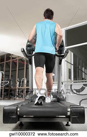 Stock Image - Rear view of a man walking on a treadmill. Fotosearch
