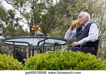 Senior man sitting on chair and drinking juice View Large Photo Image Stock Photo - Senior man sitting on chair and drinking juice. Fotosearch