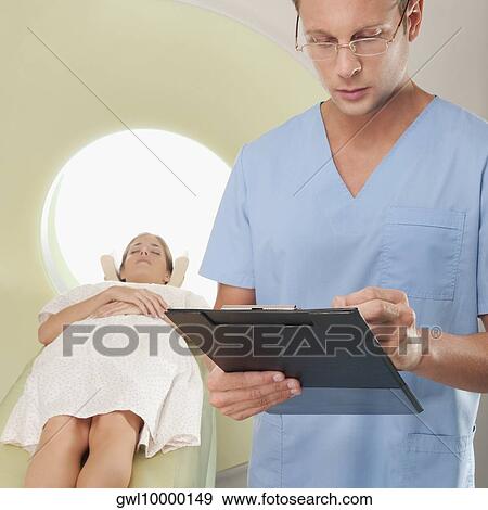 Surgeon checking medical report with a patient undergoing an MRI scan in background View Large Photo Image Stock Photo - Surgeon checking medical report with a patient undergoing an MRI scan in background. Fotosearch