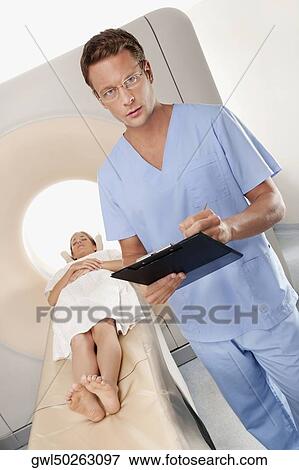 Surgeon checking medical report with a patient undergoing an MRI scan in background View Large Photo Image Stock Photo - Surgeon checking medical report with a patient undergoing an MRI scan in background. Fotosearch