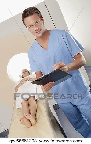 Surgeon checking medical report with a patient undergoing an MRI scan in background View Large Photo Image Stock Photo - Surgeon checking medical report with a patient undergoing an MRI scan in background. Fotosearch