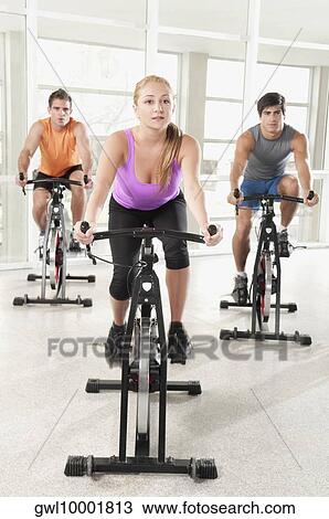 Three people working out on exercise bikes in a gym View Large Photo Image Stock Image - Three people working out on exercise bikes in a gym. Fotosearch