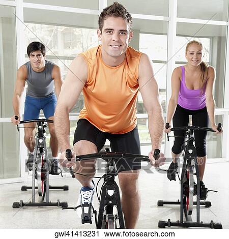 Three people working out on exercise bikes in a gym View Large Photo Image Stock Image - Three people working out on exercise bikes in a gym. Fotosearch