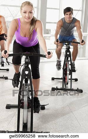 Stock Photo - Three people working out on exercise bikes in a gym. Fotosearch