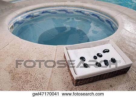 Stock Image - Towel and pebbles in a basket beside a hot tub. Fotosearch
