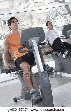 Two men working out on exercise bikes in a gym View Large Photo Image Stock Image - Two men working out on exercise bikes in a gym. Fotosearch