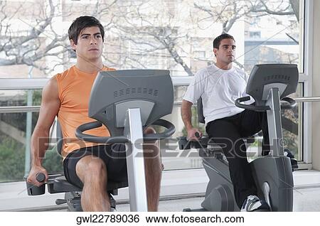 Two men working out on exercise bikes in a gym View Large Photo Image Stock Photograph - Two men working out on exercise bikes in a gym. Fotosearch