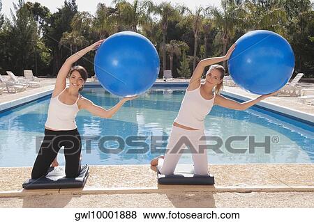Stock Photo - Two women exercising with fitness balls at the poolside. Fotosearch
