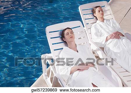 Stock Photo - Two women resting on lounge chairs at poolside. Fotosearch