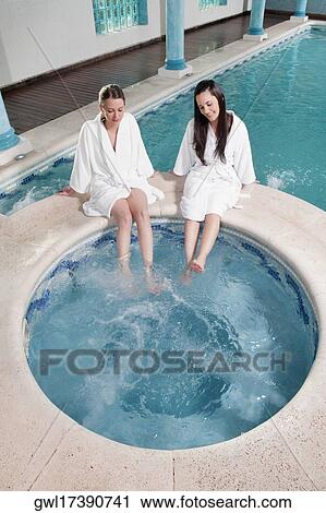 Two women sitting at the poolside with their feet soaking in water View Large Photo Image Stock Image - Two women sitting at the poolside with their feet soaking in water. Fotosearch