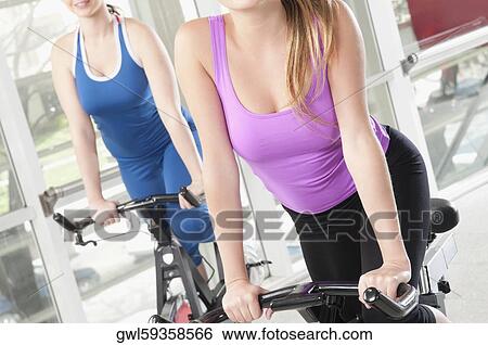 Two women working out on exercise bikes in a gym View Large Photo Image Stock Photograph - Two women working out on exercise bikes in a gym. Fotosearch