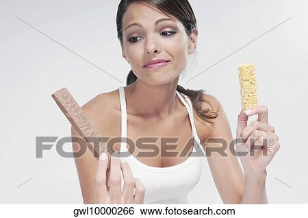 Woman choosing between a chocolate and a protein bar View Large Photo Image Stock Photograph - Woman choosing between a chocolate and a protein bar. Fotosearch