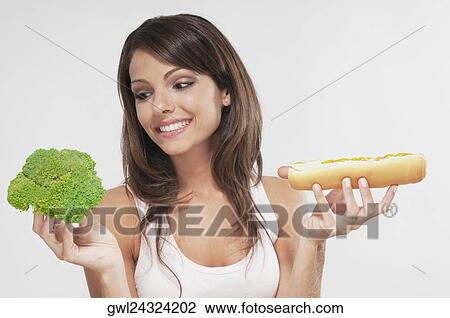 Woman choosing between broccoli and a hot dog View Large Photo Image Stock Image - Woman choosing between broccoli and a hot dog. Fotosearch