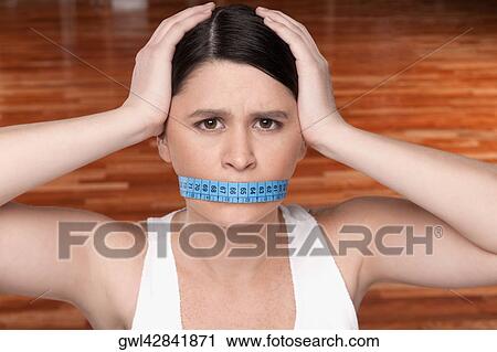 Woman covering her mouth with a tape measure View Large Photo Image Stock Image - Woman covering her mouth with a tape measure. Fotosearch
