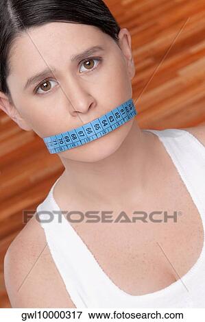Woman covering her mouth with a tape measure View Large Photo Image Stock Photo - Woman covering her mouth with a tape measure. Fotosearch