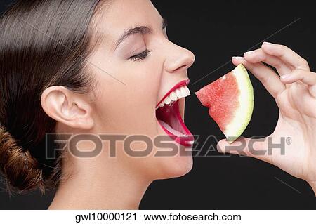 Stock Image - Woman eating a watermelon slice and smiling. Fotosearch