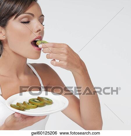 Stock Photograph - Woman eating sliced kiwi fruit. Fotosearch