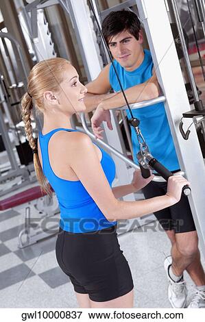 Woman exercising in a gym with a man standing beside her View Large Photo Image Stock Photo - Woman exercising in a gym with a man standing beside her. Fotosearch