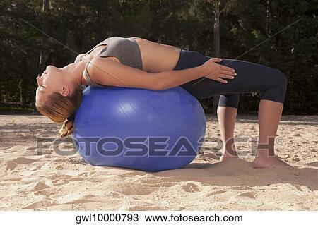 Stock Image - Woman exercising with a fitness ball on the beach. Fotosearch