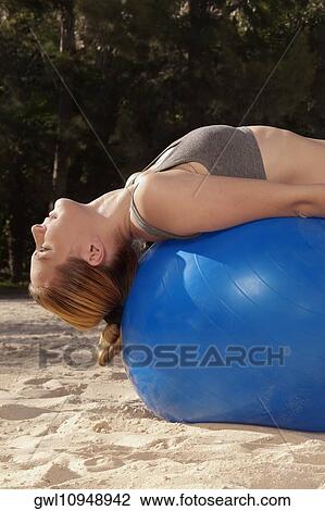Stock Image - Woman exercising with a fitness ball on the beach. Fotosearch