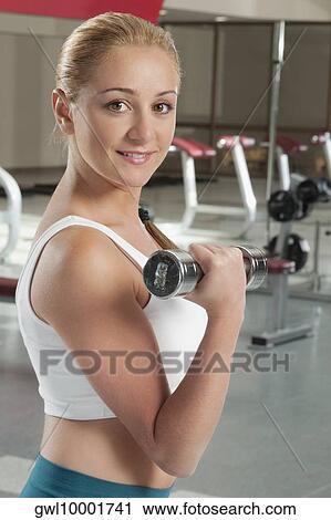 Stock Image - Woman exercising with dumbbell in a gym. Fotosearch